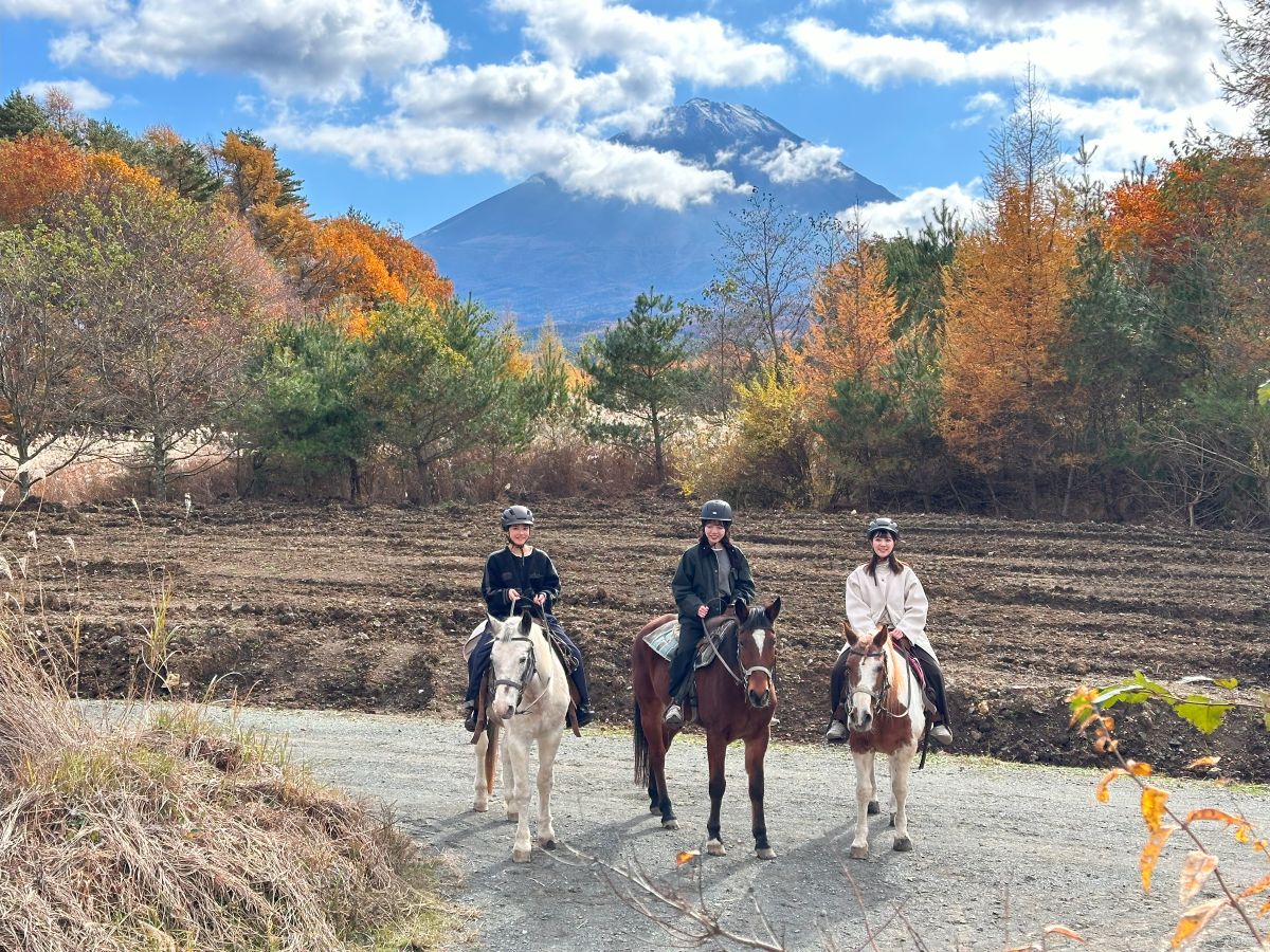 富士山と紅葉を背景に並ぶ馬と三人の乗り手